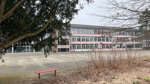 Bild von der Gesamtschule Nordstadt in Neuss mit einer roten Bank vor der Schule