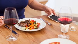 Frau am gedeckten Tisch mit Essen, Handy und Wein
