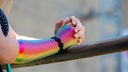 Frau mit regenbogenfarbener Unterarmbedeckung lehnt an einem Geländer.