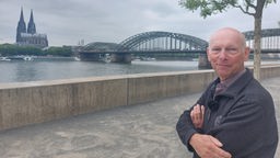 Georg Menne steht an den Rhein-Terrassen. Im Hintergrund sieht man den Kölner Dom.