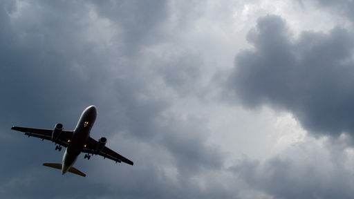 Gewitterwolken türmen sich über einem landenden Flugzeug auf.
