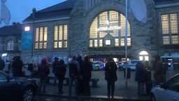 Polizeiautos stehen vor dem Bahnhof Bielefeld; Blick auf den abgesperrten Vorplatz, auf dem Menschen warten