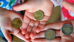 Kinderhände, die 50-Cent- und zwei Euro-Münzen zeigen