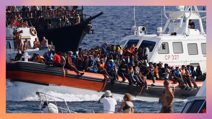 Ein Boot der italienischen Küstenwache transportiert Migranten unter der Beobachtung einer Gruppe von Touristen.