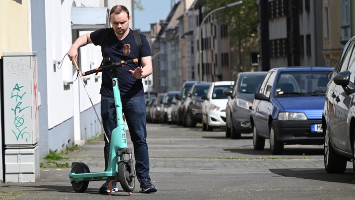 Ein blinder Mann mit einem Langstock tastet sich an einem E-Scooter vorbei