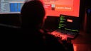 Ein Mann sitzt vor Bildschirmen, die Hacker-Programme und eine fiktive Fernlösch-Software zeigen.