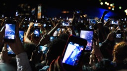 Fans halten ihre Smartphones auf einem Konzert nach oben um zu filmen