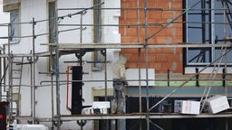  Ein Handwerker bringt in Köln auf einem Baugrundstück Dämmmaterial an einen Neubau an.