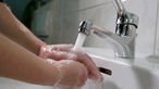 Händewaschen unter fliessendem Wasser am Waschbecken.