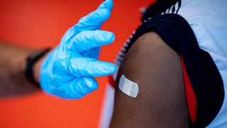 Ein Arzt klebt nach der Impfung ein Pflaster auf einen Oberarm.