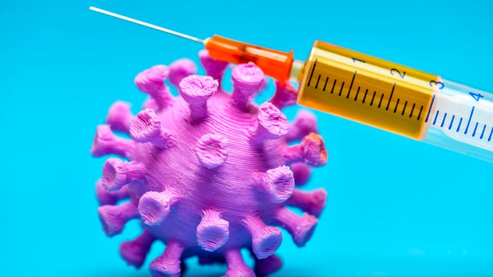 Symbolbild: Auf einem Modell des Coronavirus liegt eine Spritze
