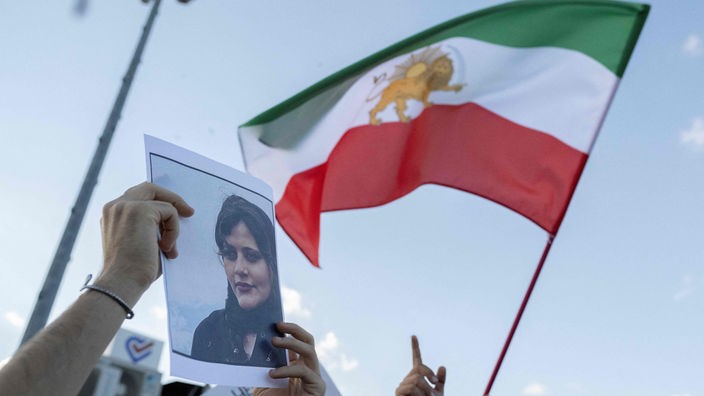 Bei einem Protest wird das Bild der verstorbenen Mahsa Amini hochgehalten, neben ihr die frühere iranische Flagge