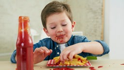 Ein Junge isst Pommes Frites mit Ketchup