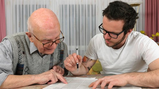Symbolbild: Junger Mann hilft Senior mit Formular
