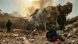 12.02.2023, Türkei, Kahramanmaras: Eine Frau sitzt neben einem eingestürzten Gebäude