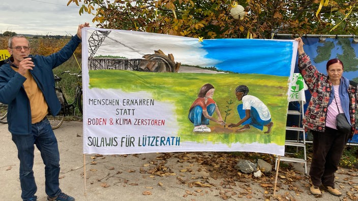 Ein Aktivist und eine Aktivistin halten ein Banner und fordern den Erhalt des Dorfes Lützerath