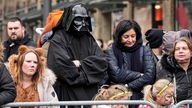 Eine Person, verkleidet als Darth Vader von Star Wars steht am Rosenmontagumzugs neben ein paar Kindern und ein paar anderen Erwachsenen.