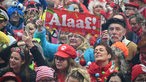 Verkleidete Menschen feiern die Sessionseröffnung am 11.11.23 in Köln. Eine Frau hält ein kleines Banner mit der Aufschrift "Alaaf!" hoch