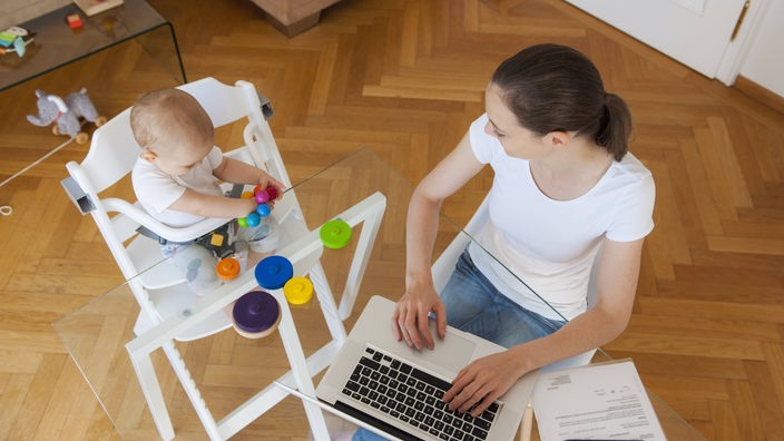 Frau sitzt mit Baby und Laptop am Tisch