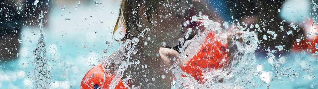 Einer junger Badegast mit Schwimmflügeln kühlt sich hohen Temperaturen in einem Schwimmbad ab.