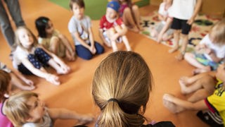 Eine Erzieherin sitzt mit Kindern im Kindergarten im Kreis auf dem Boden, in Koeln (Köln), Nordrhein-Westfalen.