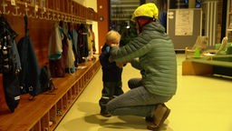 Ein Vater zieht seinem Kind im Kindergarten die Jacke aus