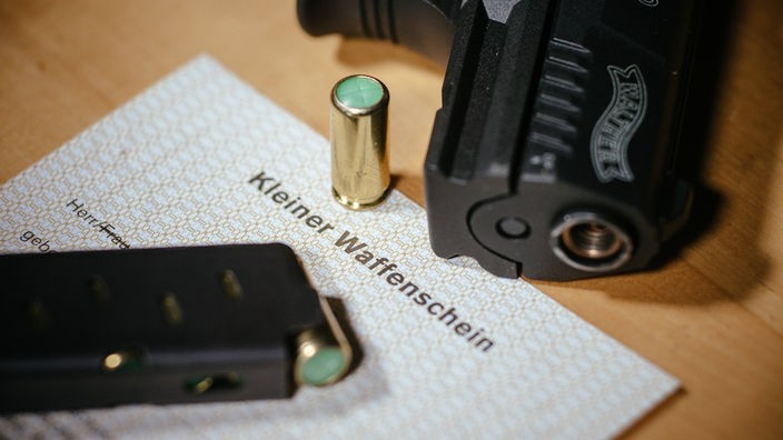 Ein Kleiner Waffenschein liegt zwischen einer Schreckschusspistole, einem Magazin und einer Knallpatrone