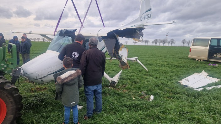Mehrere Menschen bergen das Ultraleichtflugzeug mithilfe eines Treckers von einem Feld