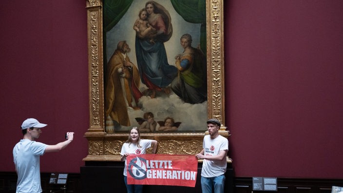  Zwei Umweltaktivisten der Gruppe ·Letzte Generation· stehen mit einem Banner in der Gemäldegalerie Alte Meister an dem Gemälde ·Sixtinische Madonna