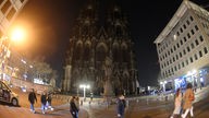 Der Kölner Dom bei Nacht ohne Beleuchtung. Im Vordergrund sind vorbei laufende Menschen zu sehen.
