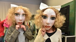 Zwei Frauen probieren riesige Theatermasken an
