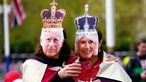 Zwei Personen posieren mit Masken, die König Charles III. von Großbritannien und Königsgemahlin Camilla darstellen.