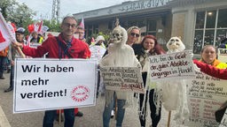 Drei Personen mit Protestschildern auf der Demo in Köln zum 1. Mai