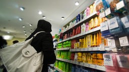 Eine Frau mit Kapuze steht vor Haarpflegemitteln in Regalen in einem Drogeriemarkt.