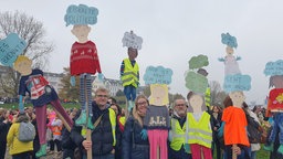 Demonstrierende halten selbstgebaute Puppen mit Sprüchen gegen Sozialkürzungen in die Höhe