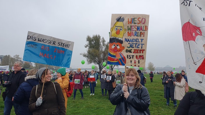 Junge Frau hält ein gemaltes Plakat hoch mit Ernie und Bert und dem Spruch: "Wieso weshalb warum. Handeln jetzt, die Zeit ist um!"