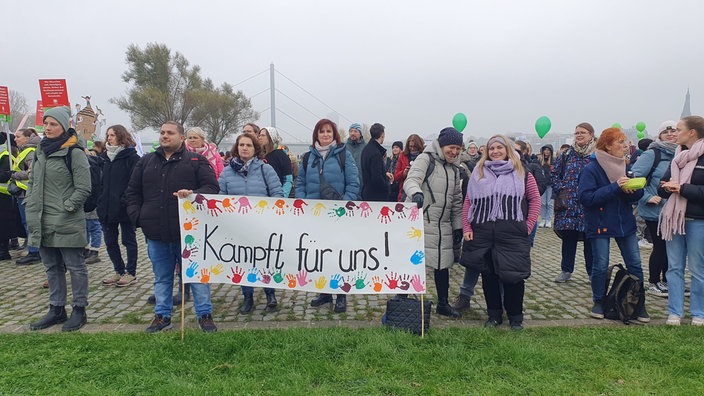 Frauen und Männer stehen hinter einem Plakat mit der Aufschrift "Kämpft für uns!"