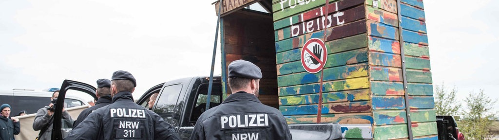 07.10.2018, Nordrhein-Westfalen, Kerpen: Einsatzkräfte der Polizei stehen neben einem auf einen Wagen geladenen Bretterhaus aus dem Hambacher Forst. Das Haus kommt nun ins Museum. Das Bonner Haus der Geschichte baut seine Dauerausstellung um.