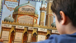 Ein Junge betrachtet ein Schaubild mit dem Titel "Die fünf Säulen des Islam"