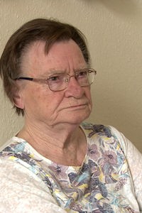 Eine ältere Frau mit Brille und kurzen dunklen haaren sitzt am Tisch