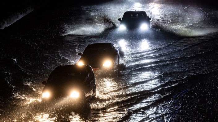 Nächtliche Aufnahme von der wasserüberfluteten A59 in Duisburg: Nach starken Regenfällen fahren Autos durch das Wasser