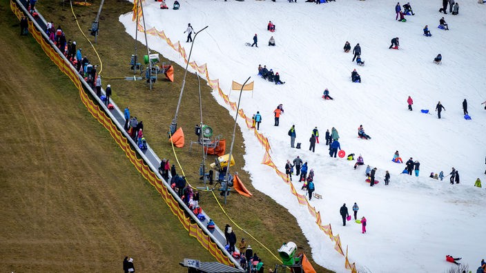 Winterberg im Sauerland: Am 3.1.2023 treiben Menschen auf einem Streifen Schnee Wintersport, daneben ist viel Grün zu sehen. 