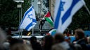 Szene aus Bochum: Ein Man trägt eine palästinensische Fahne, im Vordergrund sind zwei israelische Fahnen zu sehen und unscharf eine Menschenmenge. 