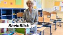NRW-Schulministerin Dorothe Feller (CDU) sitzt in einem leeren Kalssenraum und hat hinter einen Stapel Schulbücher ein Buch aufgeschlagen