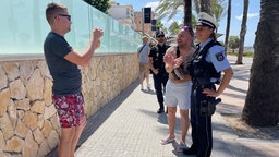 Eine Polizistin in deutscher Uniform steht neben einem deutschen Touristen mit nacktem Oberkörper, ein Mann macht ein Foto der beiden.