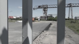 Durch ein Brückengeländer hindurch sieht man Container, die im Düsseldorfer Hafen stehen.