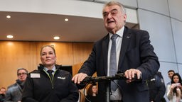 Innenminister in Nordrhein-Westfalen, lässt sich von der Polizistin Nicole Sutschet (l) einen Trainingssimulator für E-Scooter erklären.