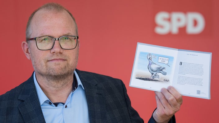 Der SPD-Fraktionschef im Landtag, Jochen Ott, hält eine Broschüre mit Karikaturen zu einem Jahr Schwarz-Grün hoch