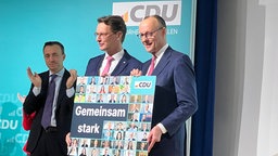 Wüst und Merz stehen auf der Bühne und halten gemeinsam ein Plakat hoch