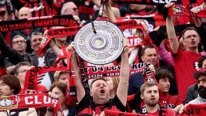 Ein Fan von Bayer Leverkusen hält die Nachbildung einer Meisterschale in den Händen